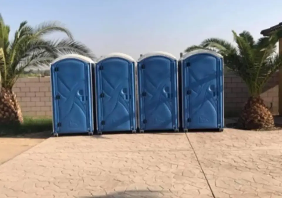 Four blue porta potties in a row on open ground