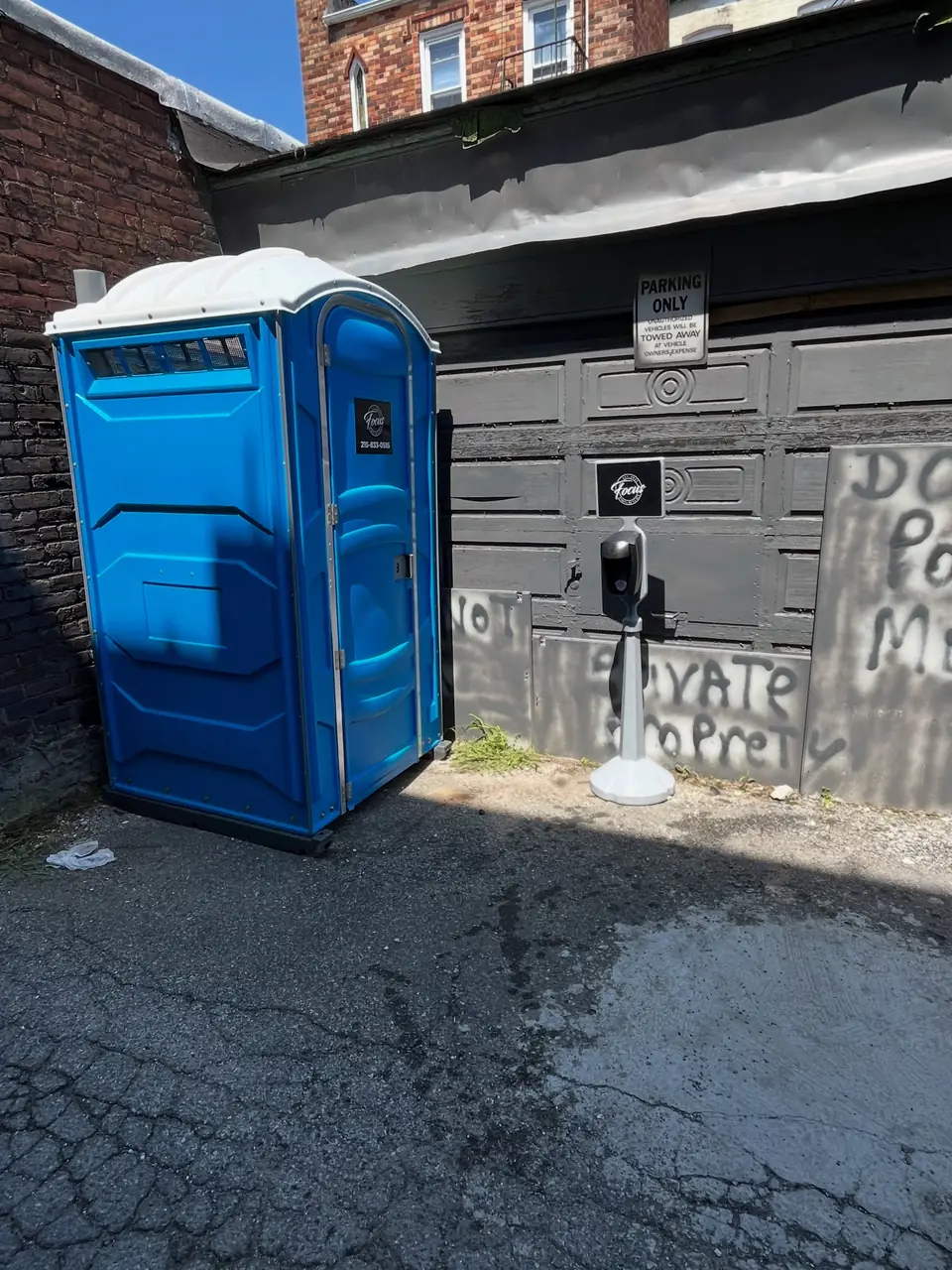 Blue porta potty and handwashing station beside a garage