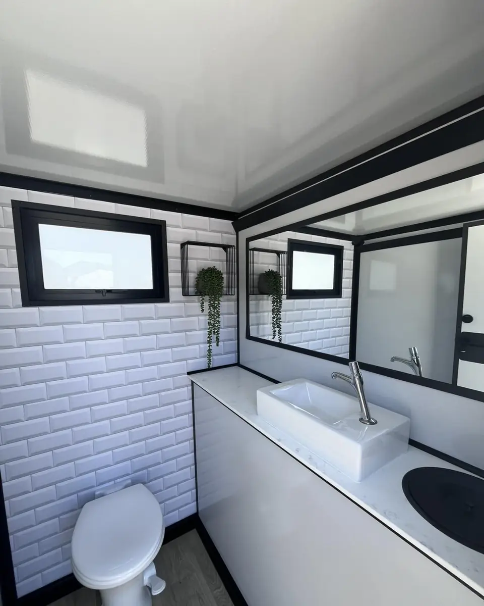 Inside a restroom trailer with tile walls, a sink, mirror and toilet