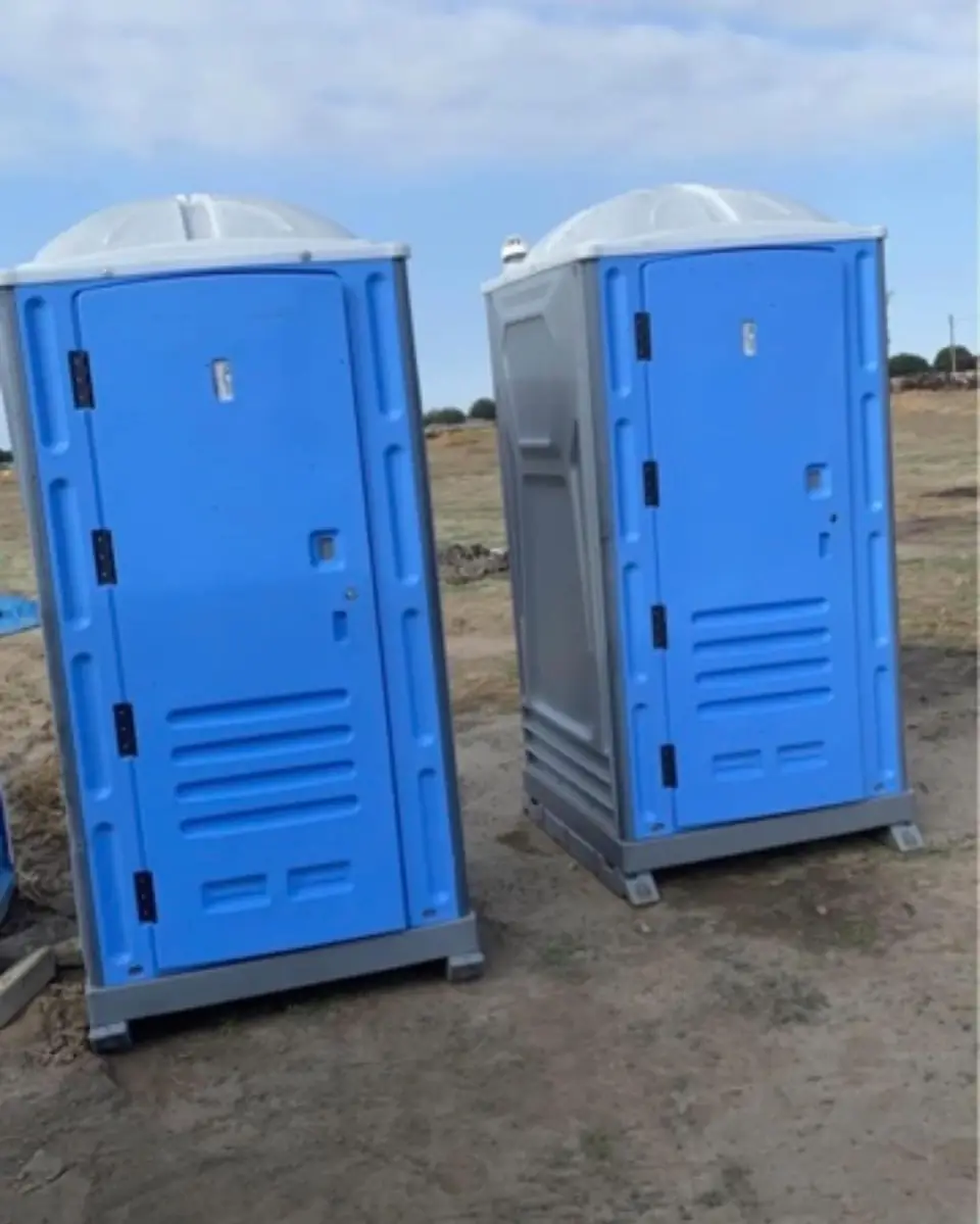 Two blue porta potties on a graded construction lot