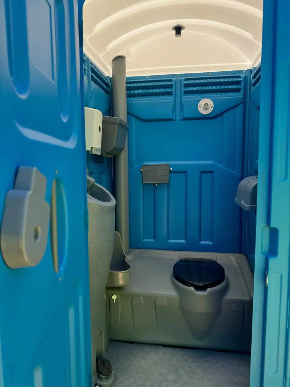 Inside a blue standard porta potty showing the seat, urinal and vent pipe