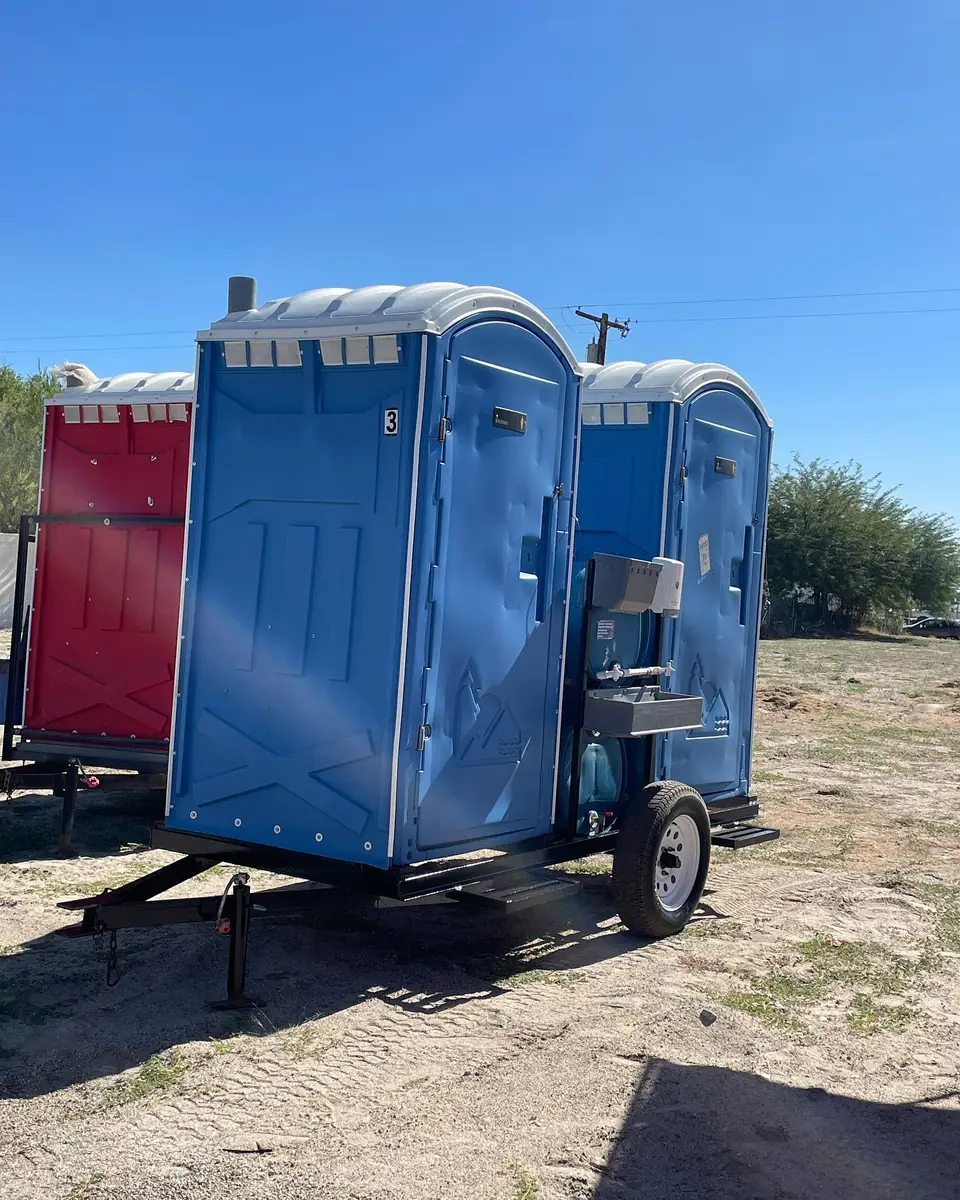 Blue porta potty mounted on a small towable trailer with a sink